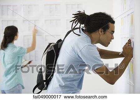 Male college student at bulletin board copying information View Large Photo Image Stock Photo - Male college student at bulletin board copying information. Fotosearch