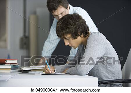Male college student working with teacher's assistance View Large Photo Image Stock Photo - Male college student working with teacher's assistance. Fotosearch