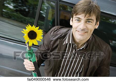 Man at gas station holding gas nozzle with sunflower emerging from end View Large Photo Image Stock Photograph - Man at gas station holding gas nozzle with sunflower emerging from end. Fotosearch