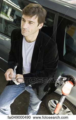 Man at gas station leaning against car waiting for gas tank to fill View Large Photo Image Stock Image - Man at gas station leaning against car waiting for gas tank to fill. Fotosearch