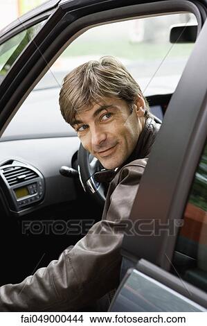 Picture - Mid-adult man getting into car, looking over shoulder before shutting door. Fotosearch