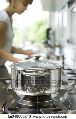 Pot cooking on stove, woman in background View Large Photo Image Stock Image - Pot cooking on stove, woman in background. Fotosearch