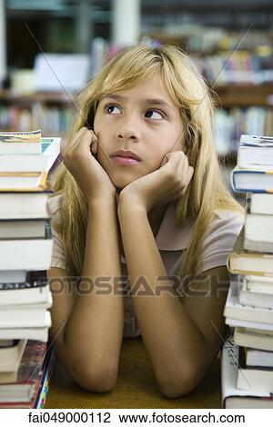Stock Image - Preteen girl sitting with two large stacks of books, chin in hands, looking away. Fotosearch