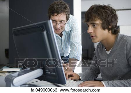 Stock Image - Teacher smiling, reviewing student's work on computer. Fotosearch