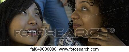 Two young women looking over shoulders at man View Large Photo Image Stock Image - Two young women looking over shoulders at man. Fotosearch