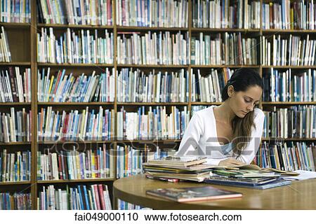 Stock Image - Woman reading book at table in library. Fotosearch