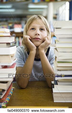 Young boy leaning on elbow daydreaming, stacks of books in foreground View Large Photo Image Stock Image - Young boy leaning on elbow daydreaming, stacks of books in foreground. Fotosearch