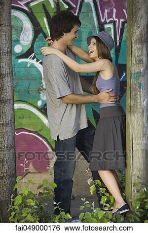 Young couple embracing in front of graffiti mural View Large Photo Image Stock Photograph - Young couple embracing in front of graffiti mural. Fotosearch