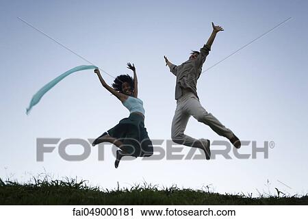 Young couple exuberantly jumping with arms raised wearing expressions of joy View Large Photo Image Stock Image - Young couple exuberantly jumping with arms raised wearing expressions of joy. Fotosearch