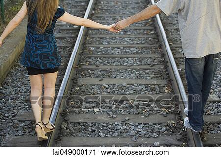 Young couple holding hands walking on rail track, rear view View Large Photo Image Stock Image - Young couple holding hands walking on rail track, rear view. Fotosearch