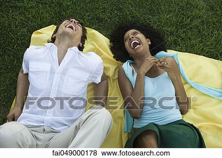 Young couple lying together on blanket on grass laughing View Large Photo Image Stock Photo - Young couple lying together on blanket on grass laughing. Fotosearch