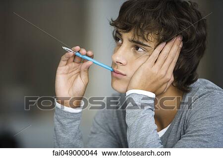 Young man daydreaming, absently holding pen in mouth View Large Photo Image Picture - Young man daydreaming, absently holding pen in mouth. Fotosearch