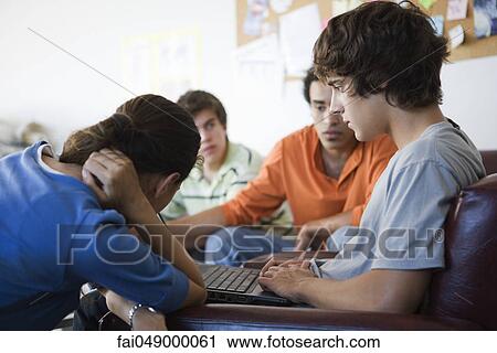 Young man using laptop, friends sitting on either side looking at display View Large Photo Image Stock Image - Young man using laptop, friends sitting on either side looking at display. Fotosearch