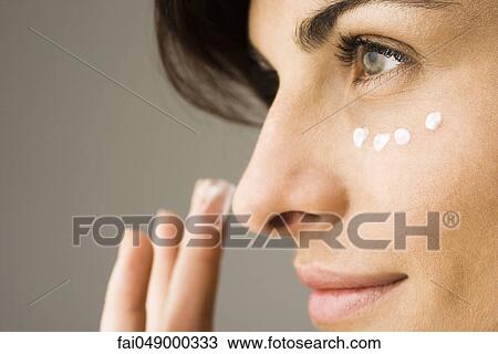 Stock Image - Young woman applying undereye cream. Fotosearch