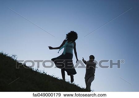 Stock Photo - Young woman playfully running away from man in pursuit. Fotosearch