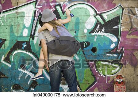 Young woman straddling companions back, spray painting graffiti mural View Large Photo Image Stock Photography - Young woman straddling companions back, spray painting graffiti mural. Fotosearch