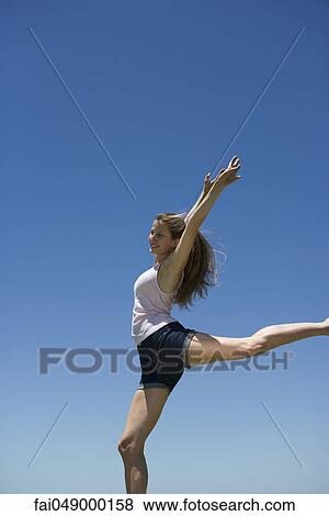 Young woman with arms raised, balancing on one leg View Large Photo Image Stock Photo - Young woman with arms raised, balancing on one leg. Fotosearch