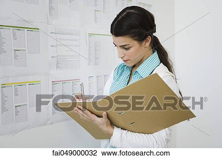 Young woman writing in notebook, standing at bulletin board View Large Photo Image Stock Image - Young woman writing in notebook, standing at bulletin board. Fotosearch