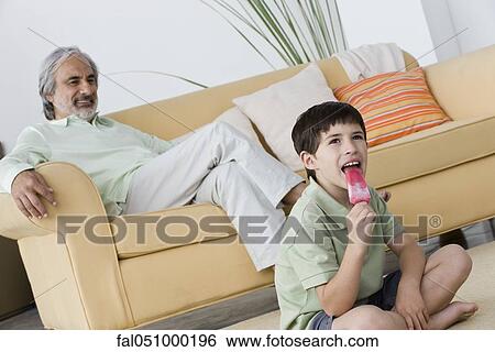 Boy eating popsicle, grandfather relaxing in background View Large Photo Image Stock Photograph - Boy eating popsicle, grandfather relaxing in background. Fotosearch