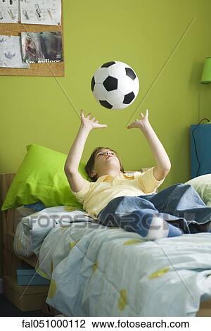 Boy lying on bed idly tossing ball into air View Large Photo Image Stock Image - Boy lying on bed idly tossing ball into air. Fotosearch