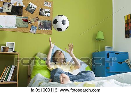 Boy lying on bed idly tossing ball into air View Large Photo Image Stock Image - Boy lying on bed idly tossing ball into air. Fotosearch