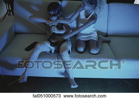 Stock Image - Brother and sister fighting over video game controller on sofa. Fotosearch