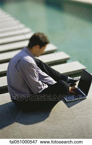Businessman sitting on ground beside pool, using laptop computer View Large Photo Image Stock Photo - Businessman sitting on ground beside pool, using laptop computer. Fotosearch