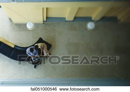 Stock Photograph - Couple sitting in lobby, using laptop computer, overhead view. Fotosearch
