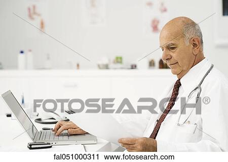 Stock Image - Doctor at desk busy with paperwork. Fotosearch