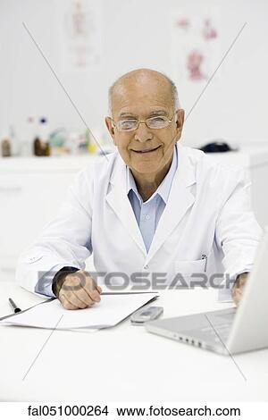 Picture - Doctor at desk completing paperwork. Fotosearch