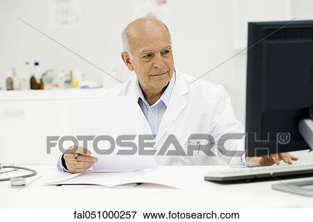 Doctor at desk completing paperwork View Large Photo Image Stock Photo - Doctor at desk completing paperwork. Fotosearch