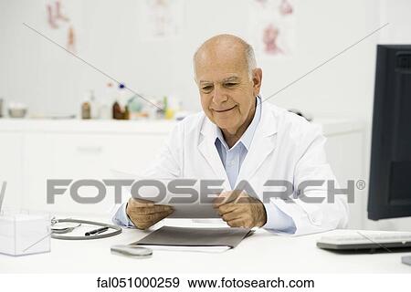 Doctor at desk reviewing paperwork View Large Photo Image Stock Photo - Doctor at desk reviewing paperwork. Fotosearch