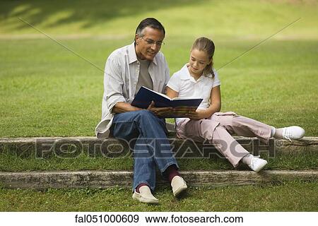 Stock Photo - Father and daughter reading together in park. Fotosearch