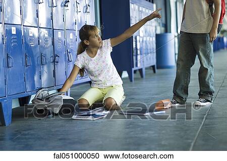 Stock Image - Female junior high student sitting on floor pointing angrily up at boy standing over her. Fotosearch