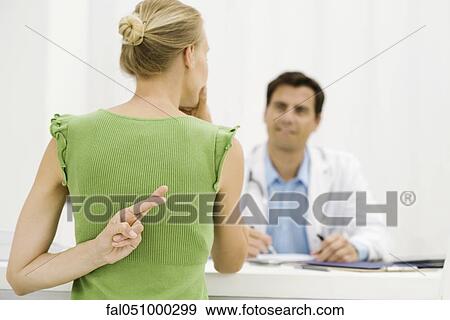 Stock Photo - Female patient with hand behind back crossing fingers, speaking with doctor. Fotosearch