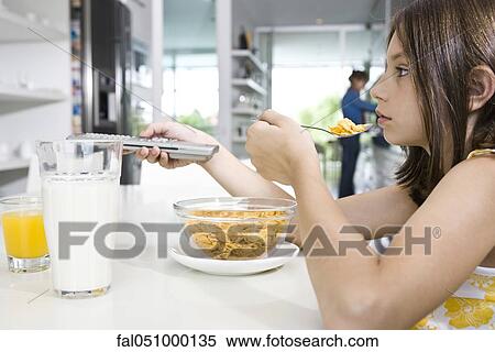 Stock Photography - Girl changing television channel while eating breakfast. Fotosearch