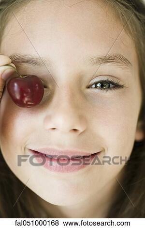 Stock Photo - Girl covering eye with cherry, close-up. Fotosearch