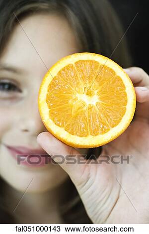 Stock Image - Girl holding up orange slice. Fotosearch
