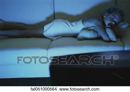 Girl lying on sofa with teddy bear, watching TV View Large Photo Image Picture - Girl lying on sofa with teddy bear, watching TV. Fotosearch
