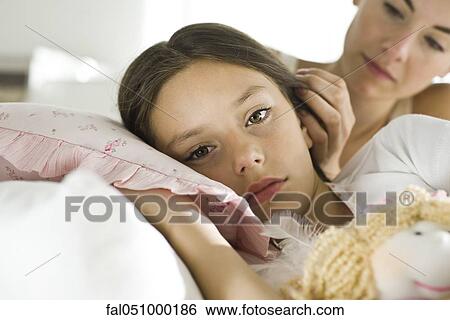 Girl resting in bed with doll, concerned mother looking on View Large Photo Image Stock Photograph - Girl resting in bed with doll, concerned mother looking on. Fotosearch