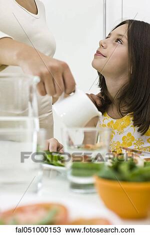 Girl sitting at table looking up at mother serving food View Large Photo Image Stock Image - Girl sitting at table looking up at mother serving food. Fotosearch