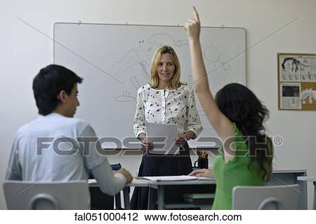 Stock Image - High school teacher in classroom, one student raising hand. Fotosearch