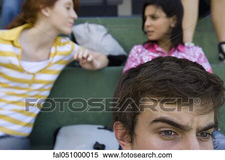 Stock Photography - Hight school friends sitting together on bleachers, boy watching intently, girls in background chatting. Fotosearch