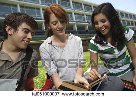 Hight school student showing friends passage in book, sitting together on school lawn View Large Photo Image Stock Photo - Hight school student showing friends passage in book, sitting together on school lawn. Fotosearch