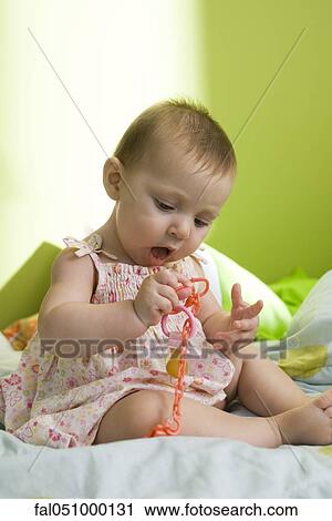 Stock Image - Infant girl holding toy chain attached to end of pacifier. Fotosearch