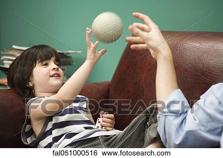 Stock Photograph - Little boy tossing ball with parent on sofa. Fotosearch