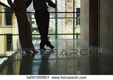 Stock Image - Male and female colleagues waiting for elevator, low angle view, backlit. Fotosearch