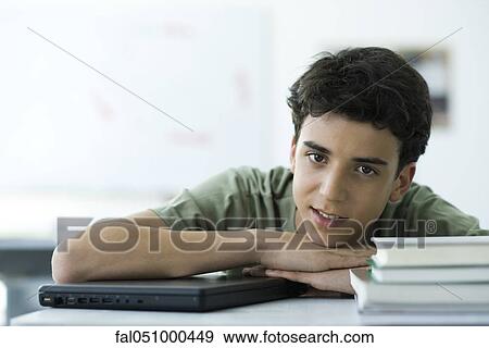 Stock Photo - Male high school student sitting at desk with head resting on arms, portrait. Fotosearch