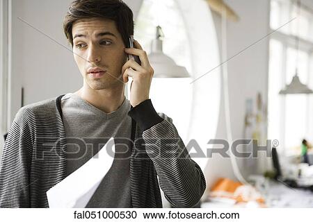 Stock Image - Man holding document on phone call. Fotosearch