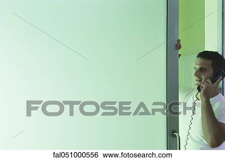 Man leaning in doorway, talking on landline phone View Large Photo Image Stock Photograph - Man leaning in doorway, talking on landline phone. Fotosearch